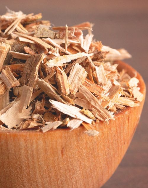 Dried white willow bark chips piled high in a small, smooth wooden bowl against a brown background.